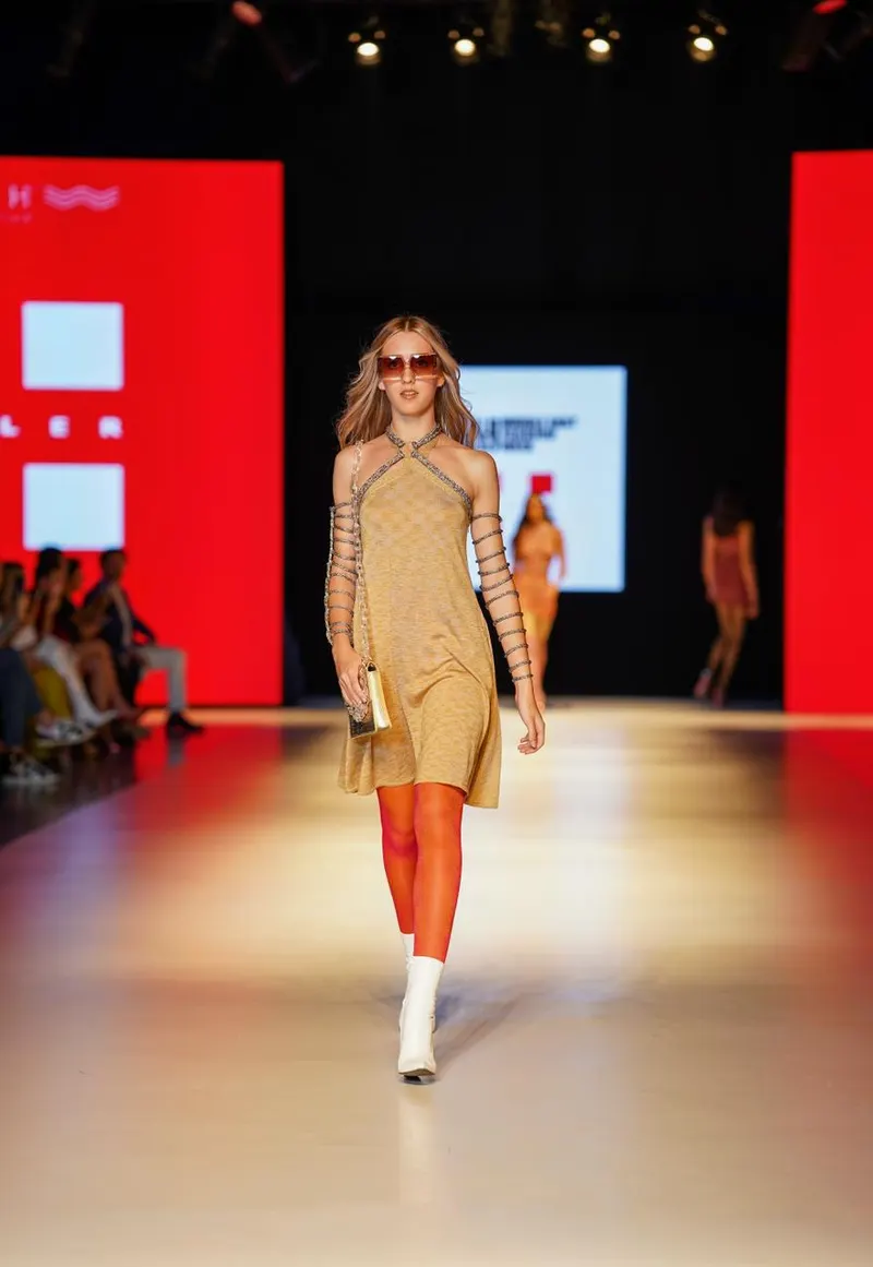 Lisa walking a runway in a camel knit dress, orange tights and white boots