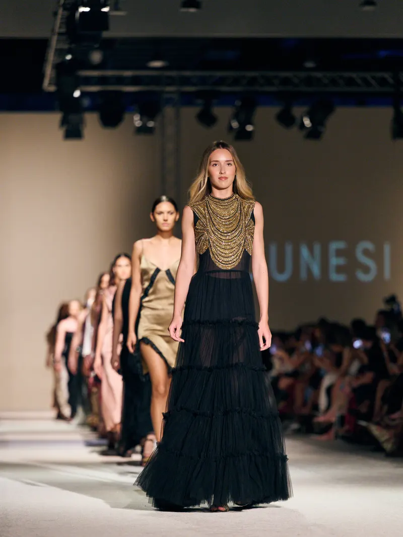 Lisa leading the Dunesi runway line in a black tiered gown with a gold beaded collar
