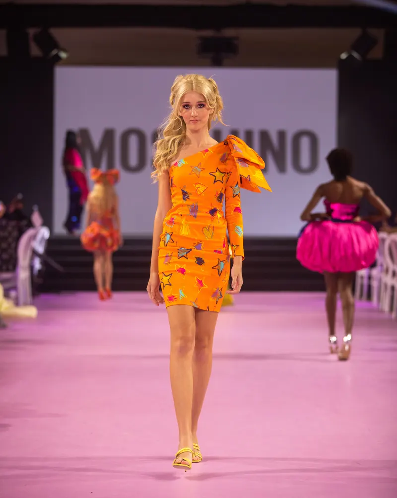 Lisa on a pink runway in an orange embellished one shoulder dress