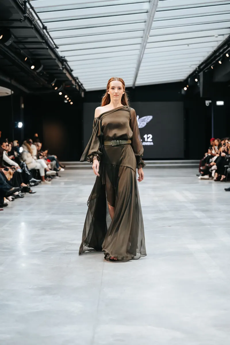 Lisa on a runway in a sheer olive one shoulder gown