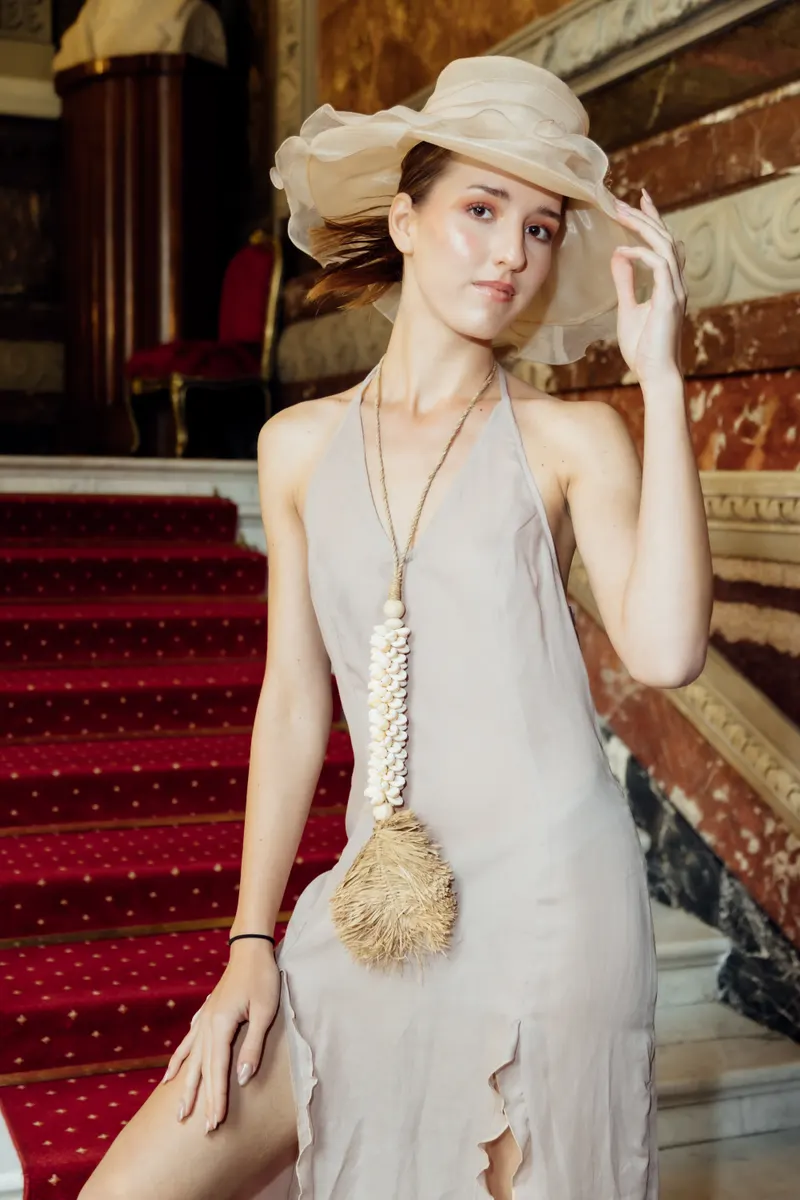 Lisa in a silk halter dress and wide brim hat on a red staircase