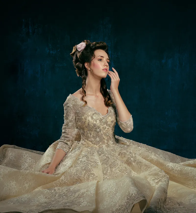 Lisa seated in a gold embroidered ball gown against dark teal