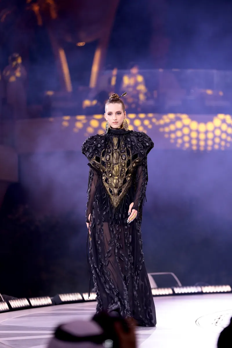 Lisa on a stage runway in a dark embellished gown with sculpted shoulders